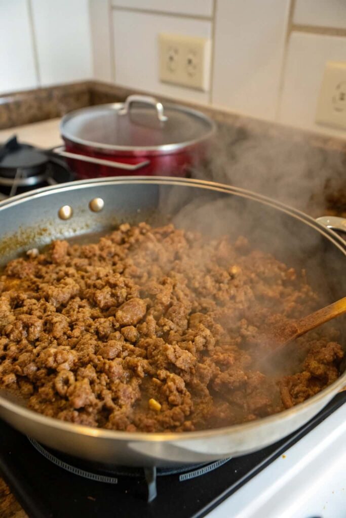 Ground beef sizzling and browning in a large pot, the first step in making cheeseburger soup.
