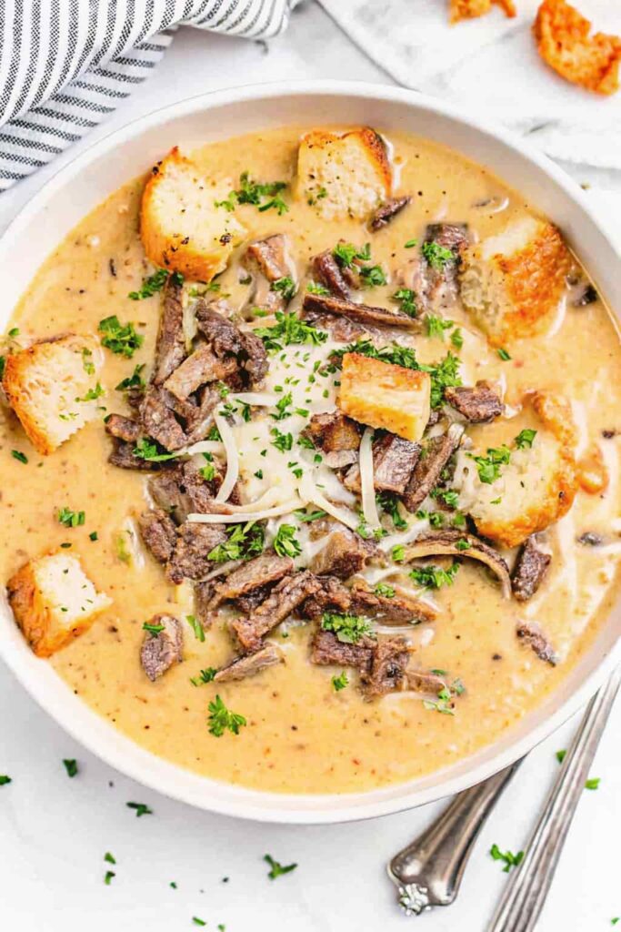 Cheesesteak soup topped with cheese and toasted croutons in a bowl